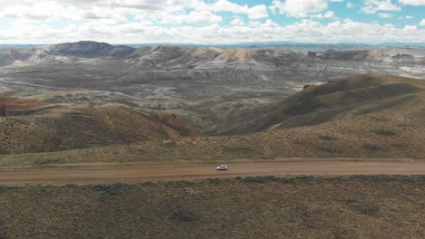 Wide-aerial-tracking-right-to-left-of-car-on-dirt-road-at-Pilot-Butte-Wild-Horse-Scenic-Loop,-Wyoming-USA-with-expansive-canyon-view