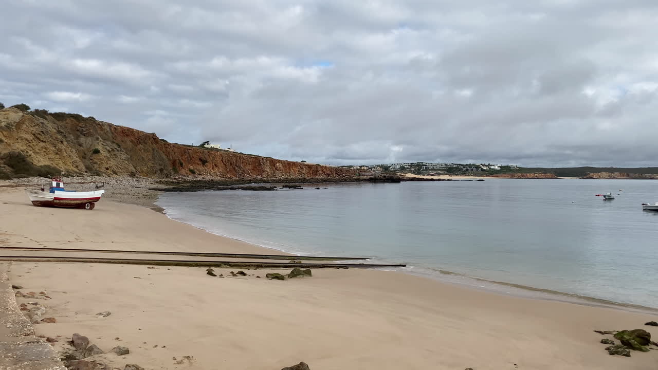 A lone sailboat floats peacefully in Sagres Bay beneath dramatic skies and the vast Atlantic cliffs