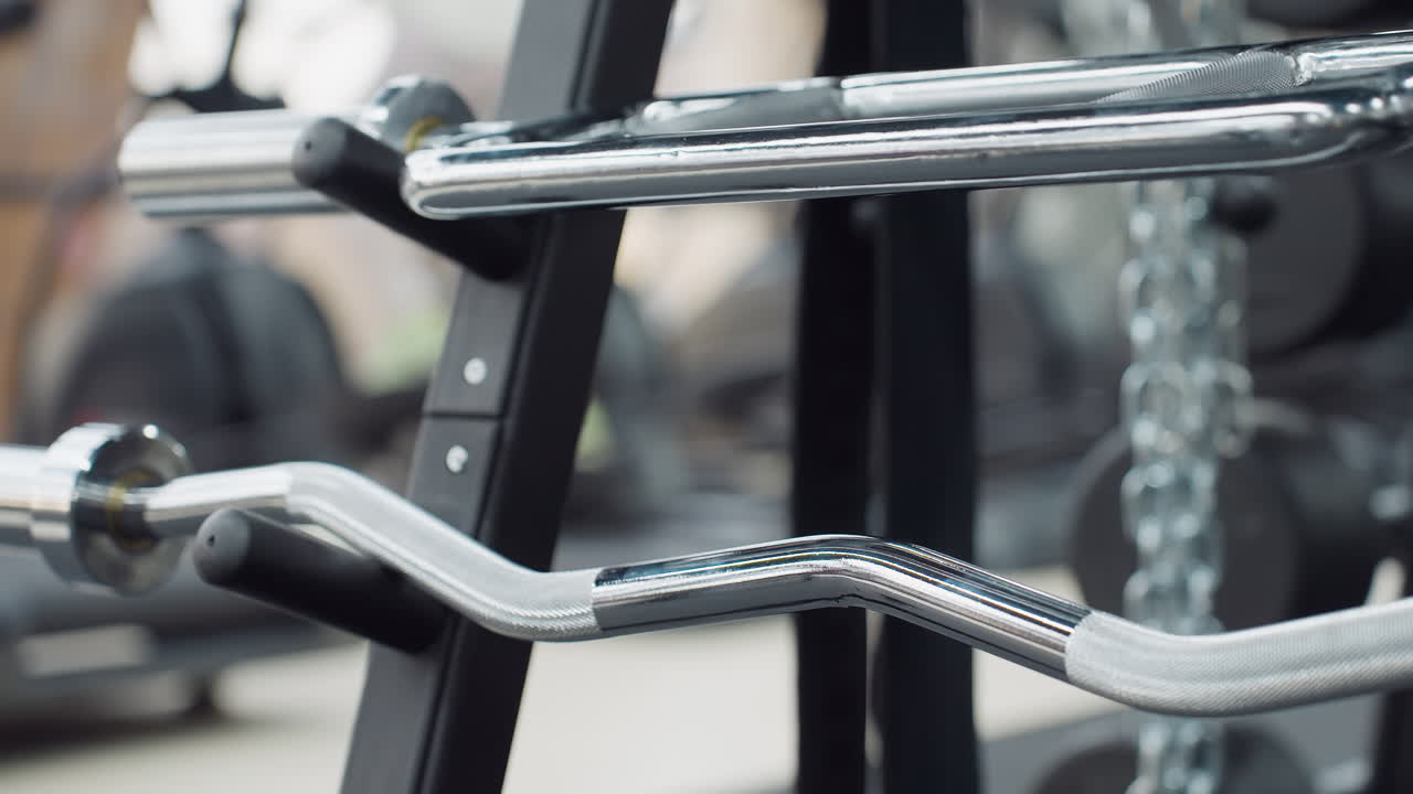 Stacked sleek chrome cable machine handles and attachments on sturdy rack in bright modern gym with blurred cardio machines and weight plates in background showcasing professional fitness environment