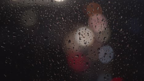Close-up-off-rain-on-a-window-at-night-with-blurred-background-street-and-traffic-light