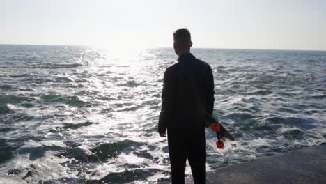 Young-man-holds-his-longboard-standing-by-the-sea