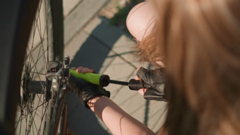 primer plano de una mujer con guantes bombeando aire en un neumático de bicicleta con boquilla verde en un día soleado, con enfoque en su mano y bomba, fondo suavemente borroso