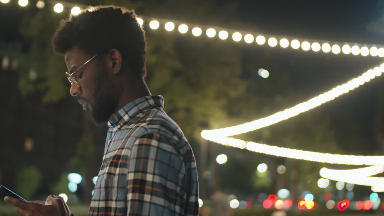 hombre afroamericano enviando mensajes por teléfono al aire libre por la noche