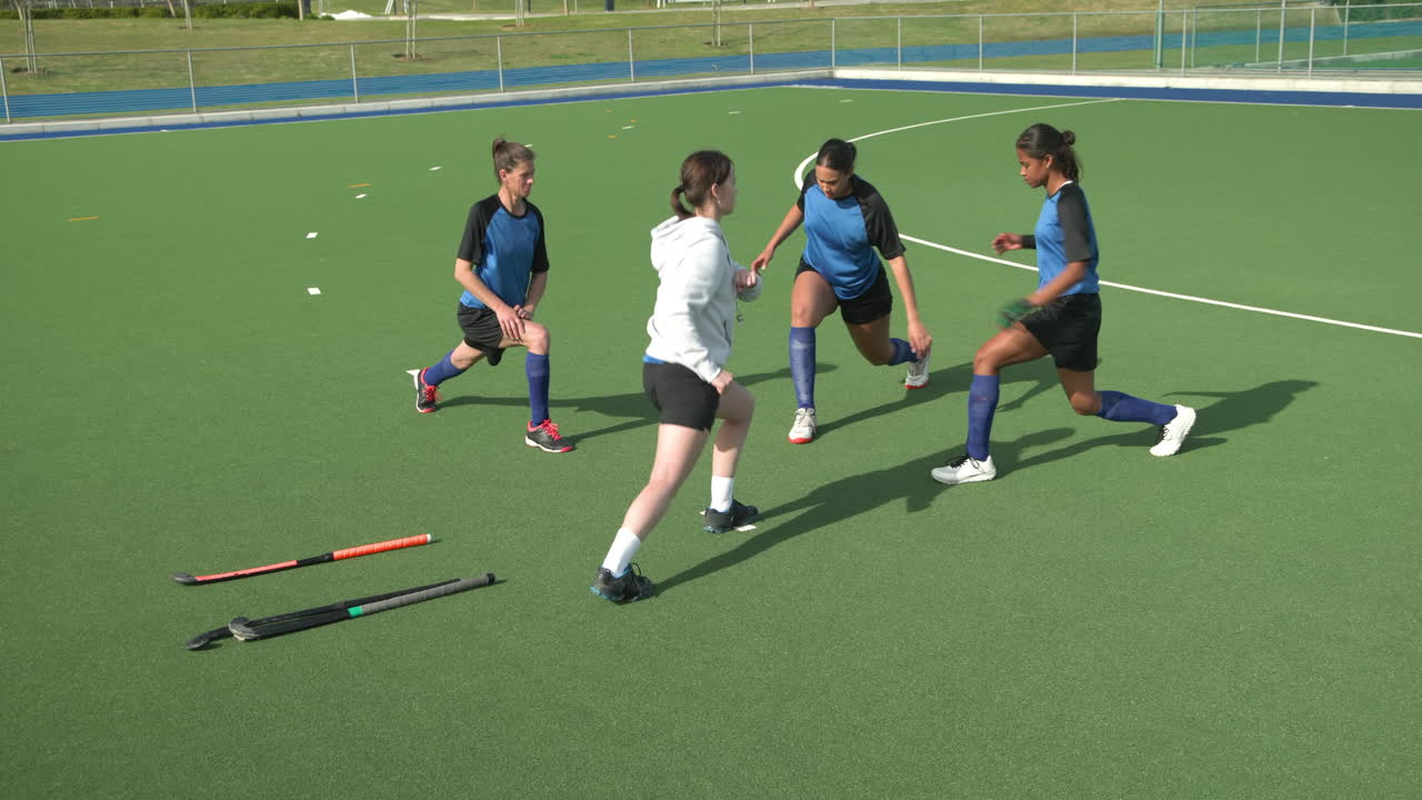 Female hockey players warming up on field, practicing lunges together