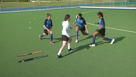 female hockey players warming up on field, practicing lunges together