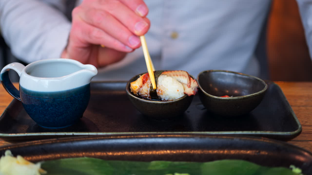 Close up of a man eating multiple nigiri from a black tray at a restaurant