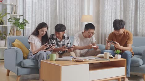 asian teen group playing game on smartphone, break time after working on online project, students with books and laptop studying at home