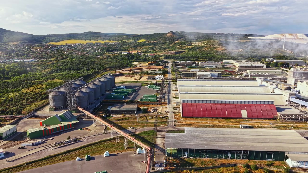Birds eye view of an industrial area with factories and silos near a green landscape in daytime