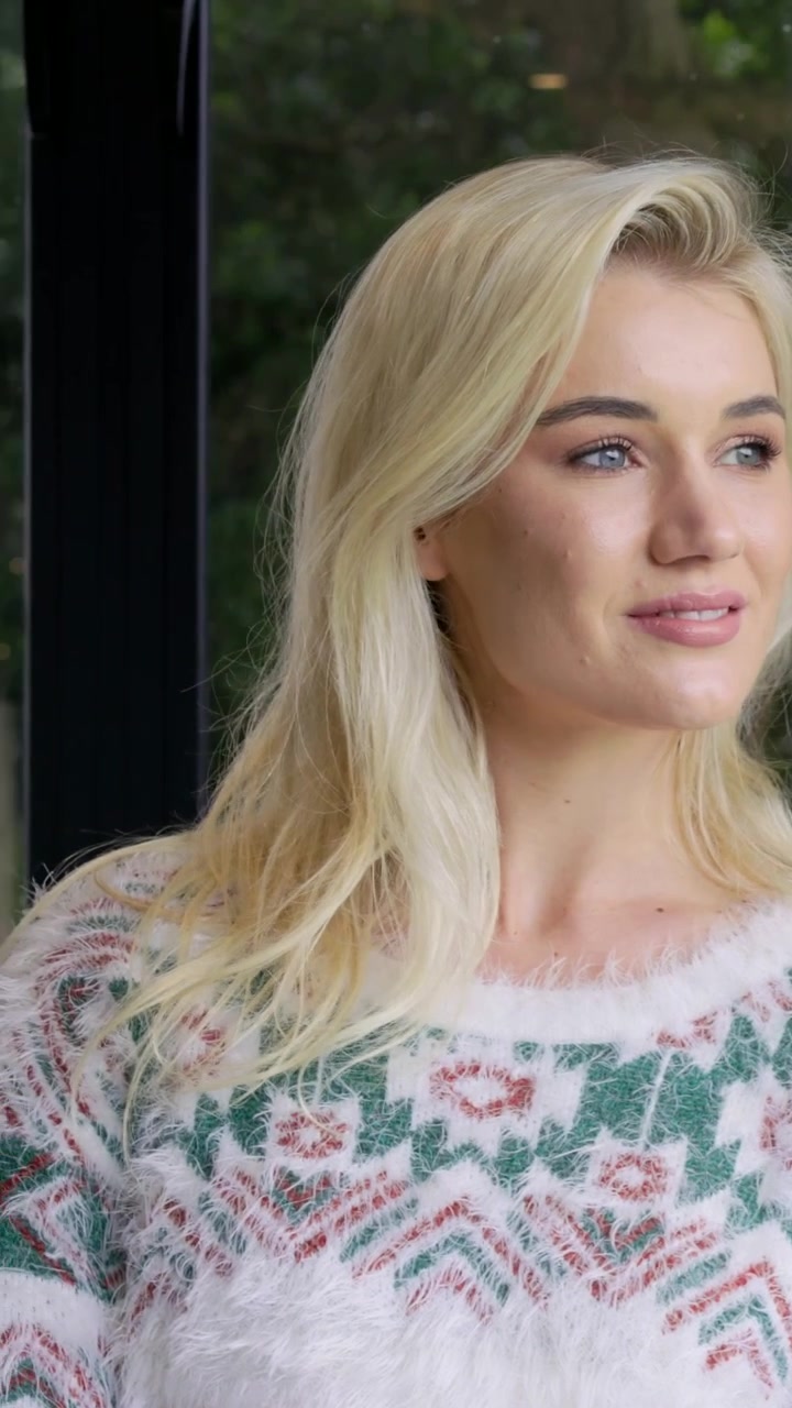Vertikal video: Kamera zoomer ind på kvinde, der vender sig for at kigge ud af billedet ved vinduet derhjemme i en blød sweater
