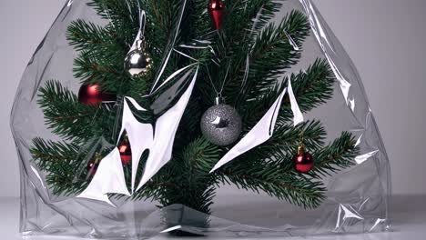 small decorated christmas tree wrapped in transparent plastic film, ready to be shipped or stored, representing consumerism, winter holidays, environmental issues and overpackaging