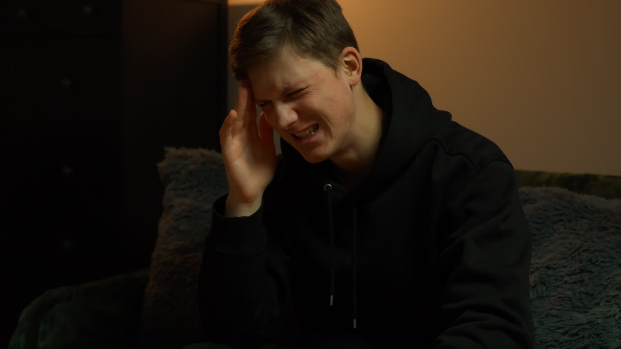 Male musician sits with head down in emotional moment reflecting stress and personal struggle indoors