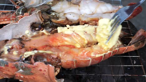 extreme close up chef uses fork to wiping butter on grilled lobster - thailand