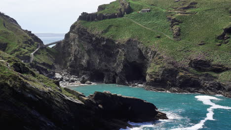 the ruins of popular tourist destination tintagel castle in cornwall on top of a cliff with new bridge that leads to the island and the bay with beach below