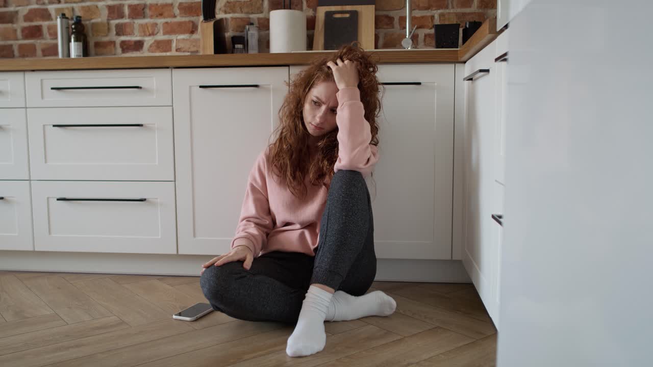 Giovane donna caucasica depressa seduta triste sul pavimento in cucina