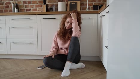 Depressed-young-caucasian-woman-sitting-sad-on-floor-in-the-kitchen