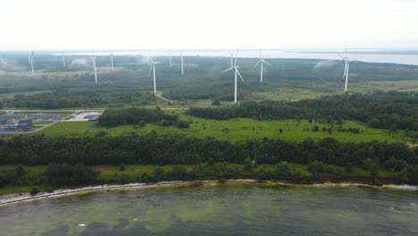 aerial drone footage orbiting around a peninsula that has a wind farm on it with large and tall renewable energy creating wind turbines during a cloudy and misty day in paldiski nature. shoreline seen