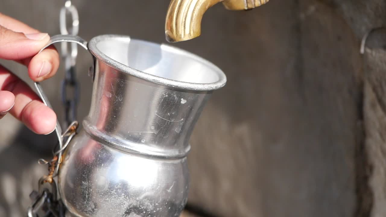 Hand filling a vintage metal cup from a public water fountain