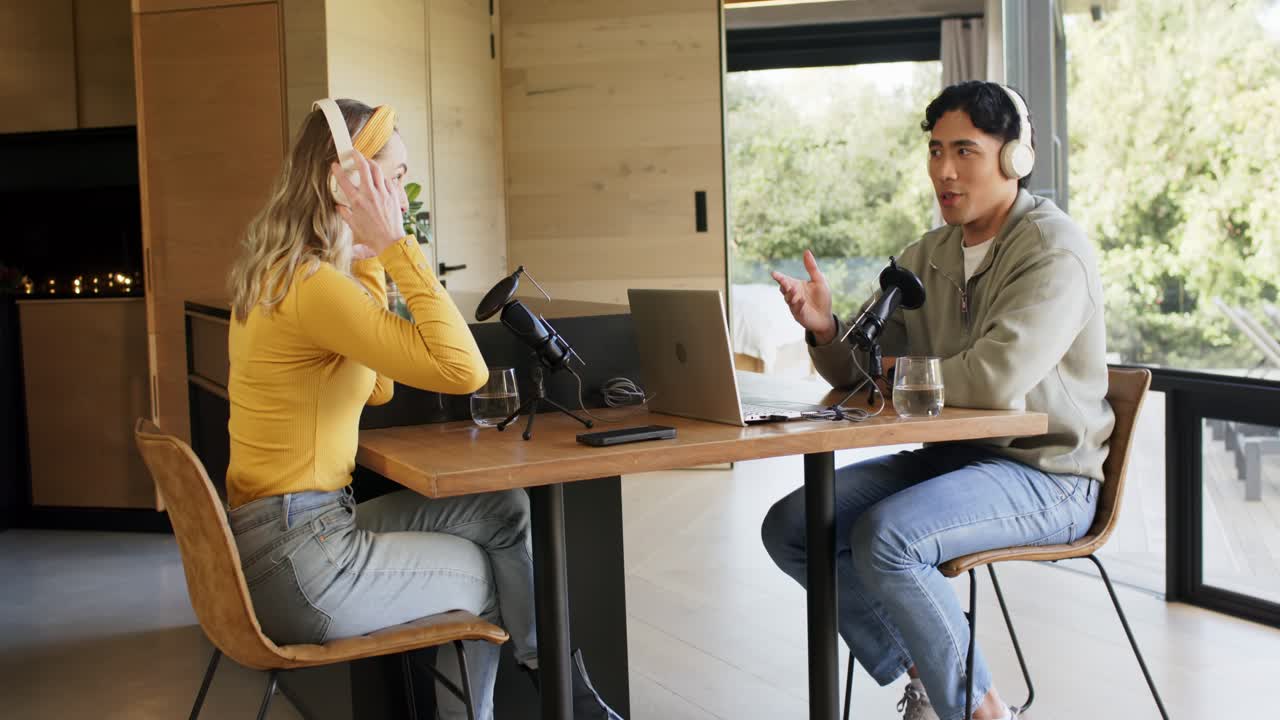 Diverse co-hosts starting podcast recording at home office table by adjusting mics, reviewing notes