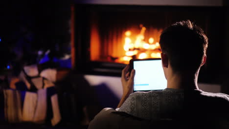 A-Man-Orders-Gifts-For-Christmas-Sitting-At-Home-By-The-Fireplace-Using-Tablet