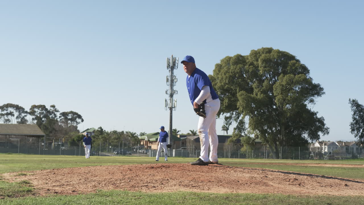 Giocatore di baseball in uniforme sul monte di lancio, con i compagni di squadra nel campo esterno.