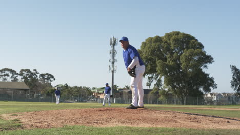 Pitching baseball, man in uniform on mound with teammates in outfield