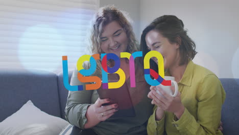 animation of lgbtq over happy caucasian lesbian couple using tablet and sitting on sofa at home