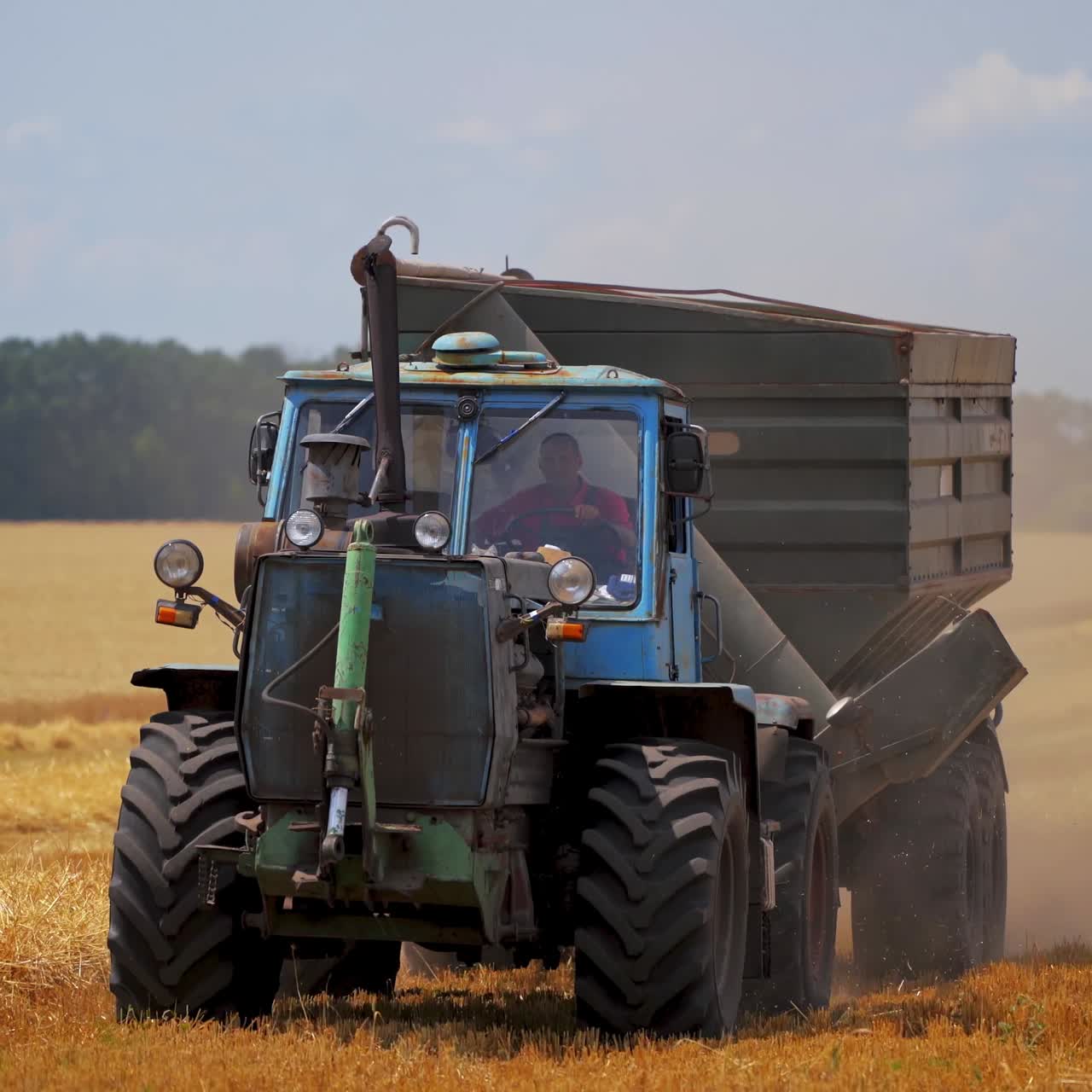 Tractor driving on field in summer. Agricultural machine working on field at harvesting season. Seasonal works in farmland