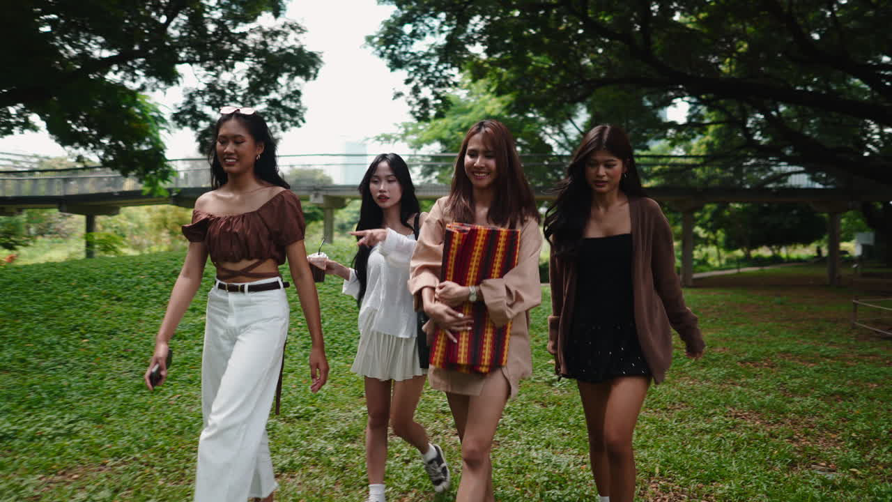 Cuatro mujeres jóvenes caminando y desplegando una manta de picnic en un parque