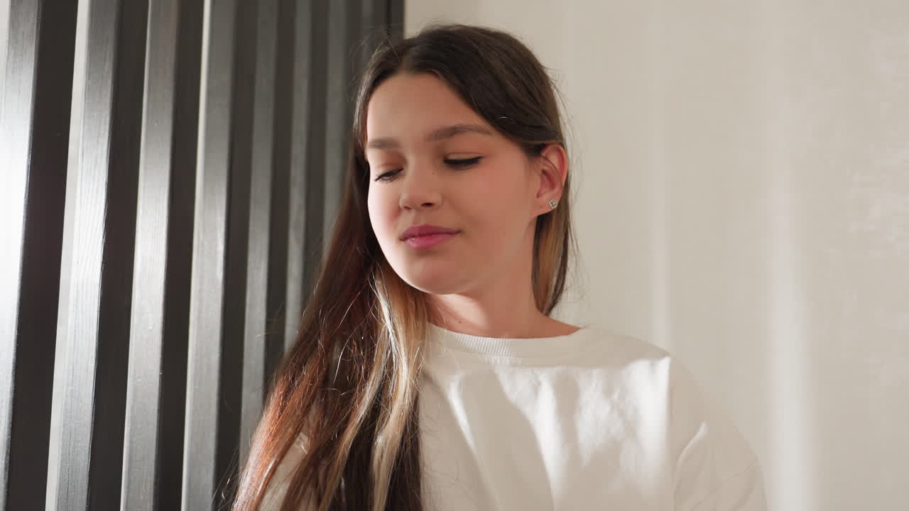School girl in striped pajamas holds leg to ear like phone, supporting foot with hands, focused expression while pretending conversation, playful bedroom moment, then lowers leg after call