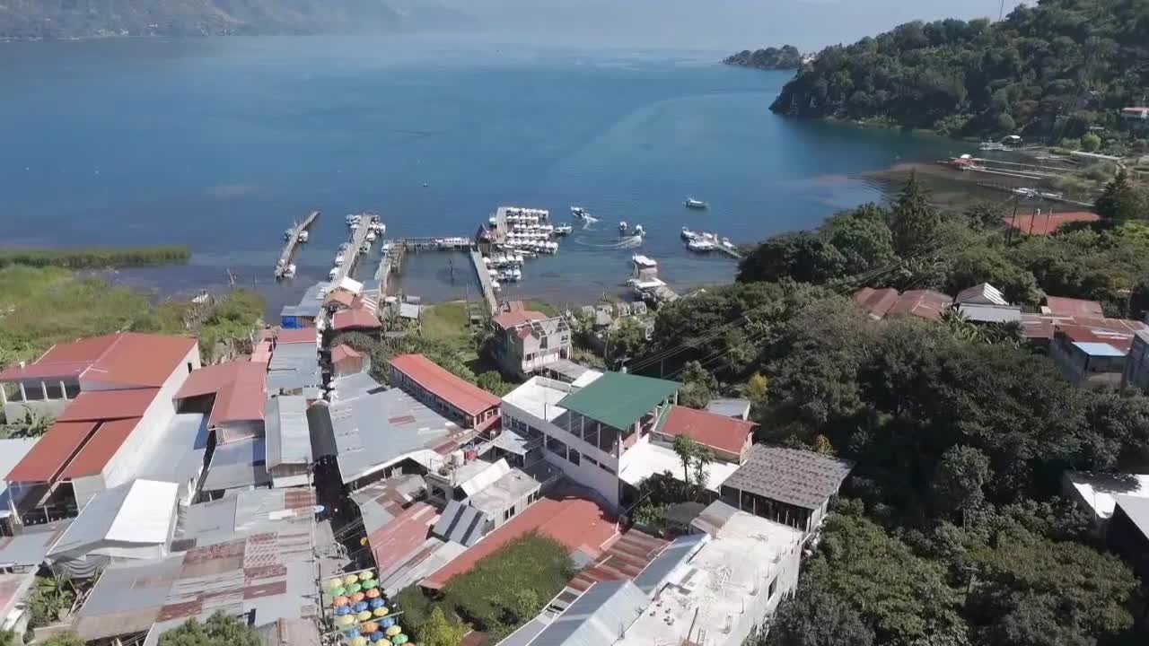 una impresionante vista aérea de san juan la laguna, una ciudad a orillas de un lago en guatemala, con coloridos edificios, muelles, barcos y exuberante vegetación a lo largo del lago atitlán.