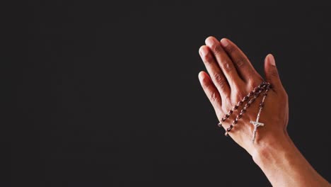 praying hands with rosary on black background with copy space