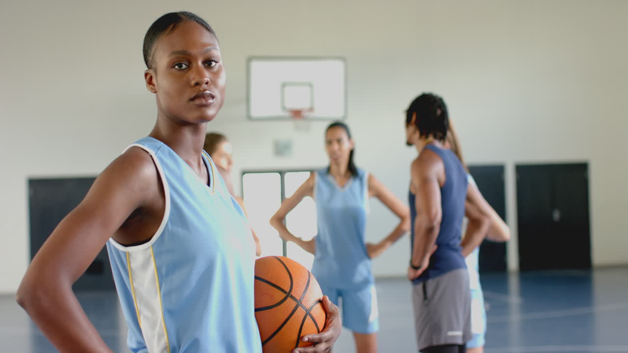 Holder basketball, kvindelig atlet står selvsikkert i en gymnastiksal med holdkammerater