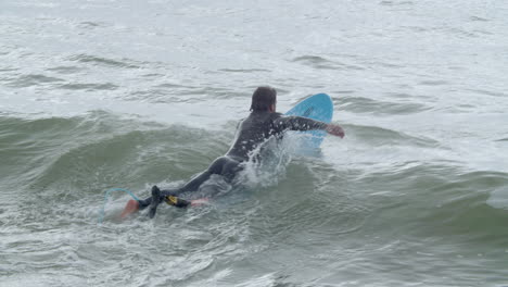 hombre deportivo en traje de neopreno con pierna artificial acostado en la tabla de surf y nadando en el océano 9