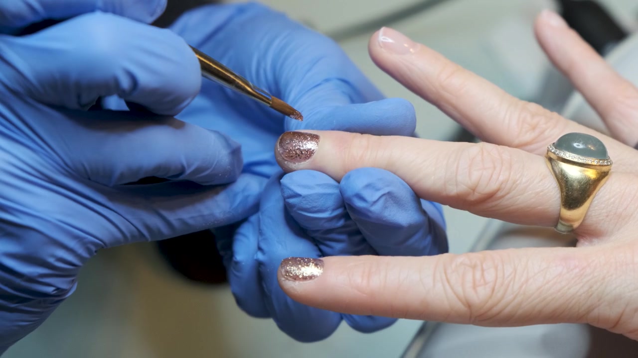 Une jeune femme riche dans un salon de beauté recevant une manucure avec un vernis à ongles doré scintillant, réalisée par une esthéticienne ongulaire