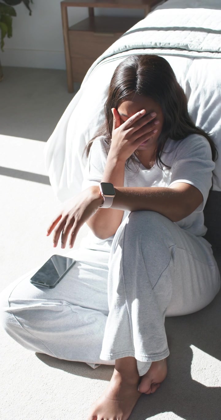Video verticale: Donna africana adulta che legge un messaggio sul telefono, controlla l'orologio e si copre il viso in camera da letto.