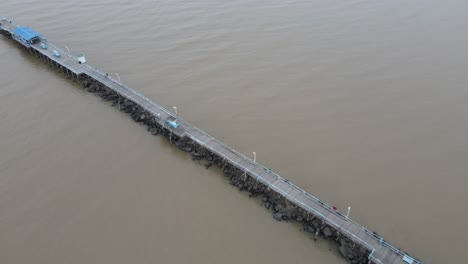 drone flying along the length of pier extending from land out over into the sea