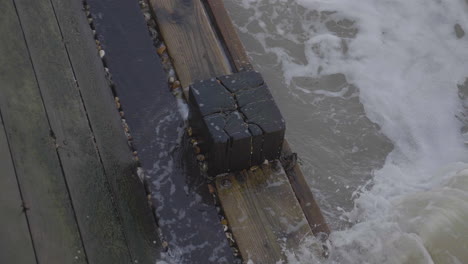 the sea flowing round a wooden pier pylon in slow motion