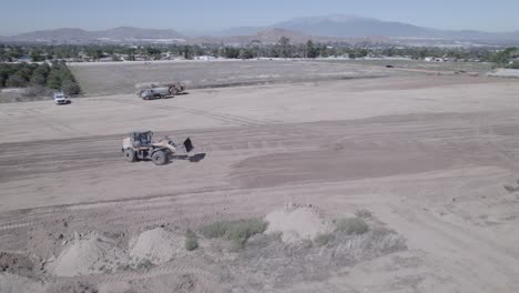 Un-Dron-Captura-El-Esfuerzo-Coordinado-Cuando-Un-Cargador-De-Ruedas-Regresa-Después-De-Arrojar-Una-Carga-De-Tierra,-Ayudando-A-Un-Cargador-De-Orugas-En-Las-Etapas-Finales-De-Aplanar-El-Terreno-Para-Un-Sitio-De-Construcción-De-Una-Nueva-Casa