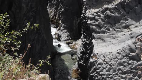 Person-standing-in-a-river-with-water-flowing-around-stones-at-Taormina,-Italy