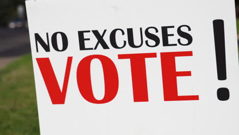 political voter rally sign next to road with cars driving by close up, no excuses vote