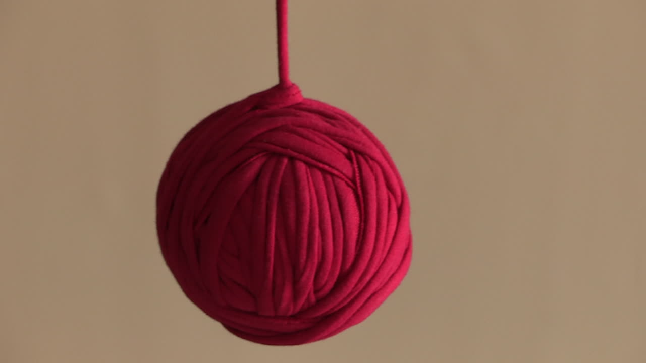 A red thread coiled into a ball shape, hanging down and sliding