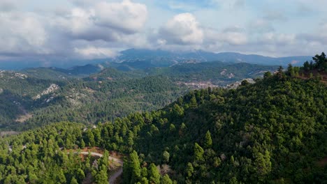 Drohnenblick-über-Einen-Grünen,-üppigen-Wald-Mit-Hohen-Berggipfeln-Und-Einem-Klaren-Blauen-Himmel-Mit-Dicken-Weißen-Wolken,-Insel-Euböa,-Griechenland