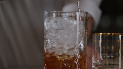 bartender stirs an old fashioned in ice in a large mixing glass