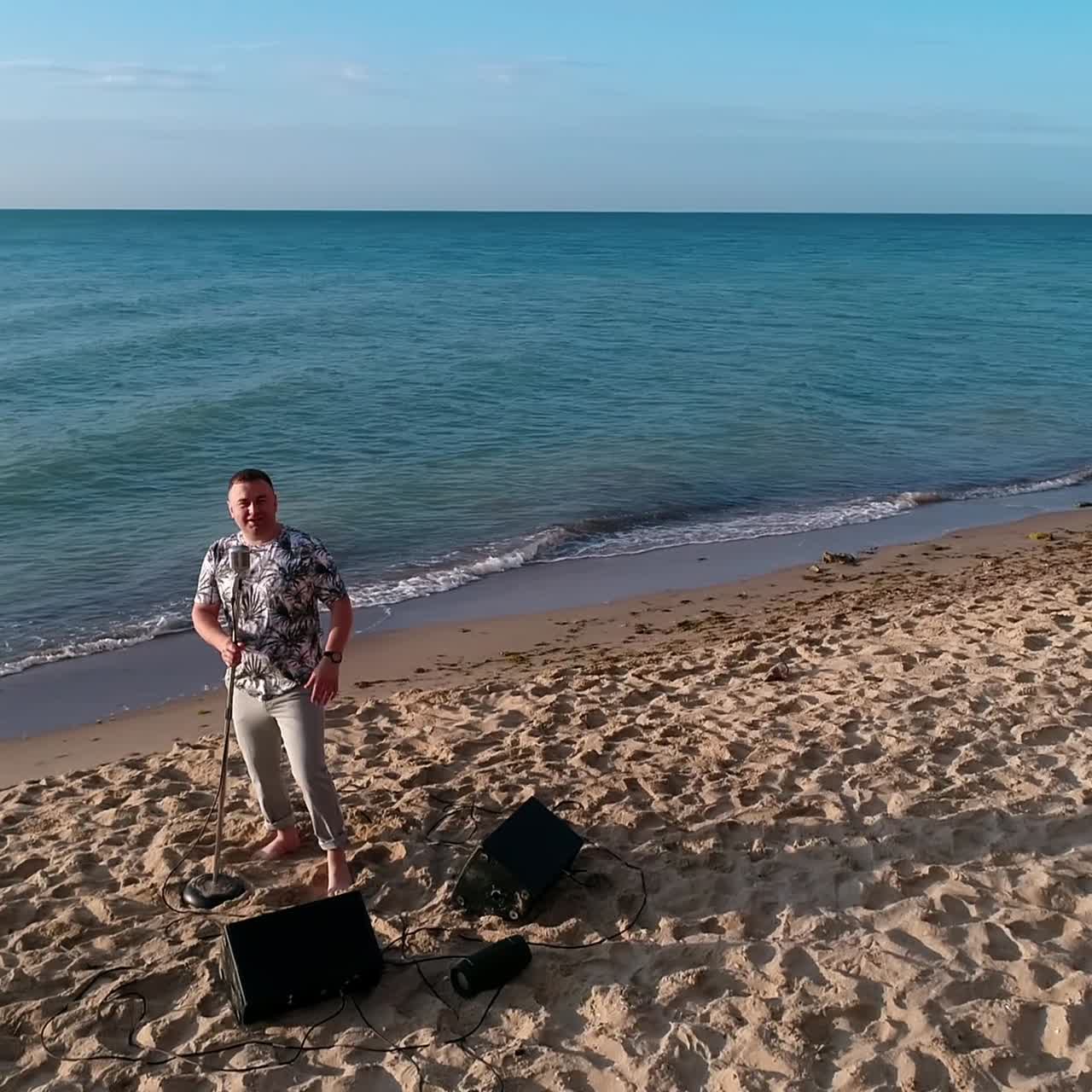 Man singing into microphone on beach. Aerial view of musician sings into the microphone on beach