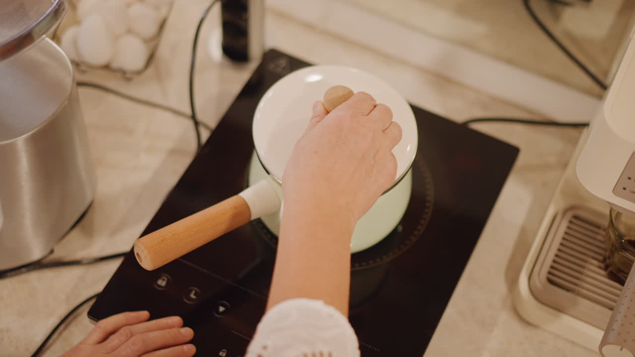 Baker seals lid while pumpkin simmers, induction cooktop display showing controls, neat countertop, enamel pot of orange pumpkin chunks simmering to soften before mashing, minimalist modern kitchen