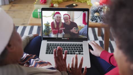 African-american-mother-and-daughter-using-laptop-for-christmas-video-call-with-family-on-screen