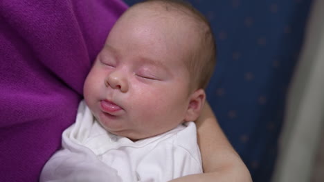 mommy's trying to wake her baby up by rubbing its cute cheek. baby continues to sleep not paying attention to mum's attempts. beautiful baby face close up.