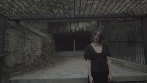 creepy pale female with dark make up and black dress looking spooky at the camera while turning her head