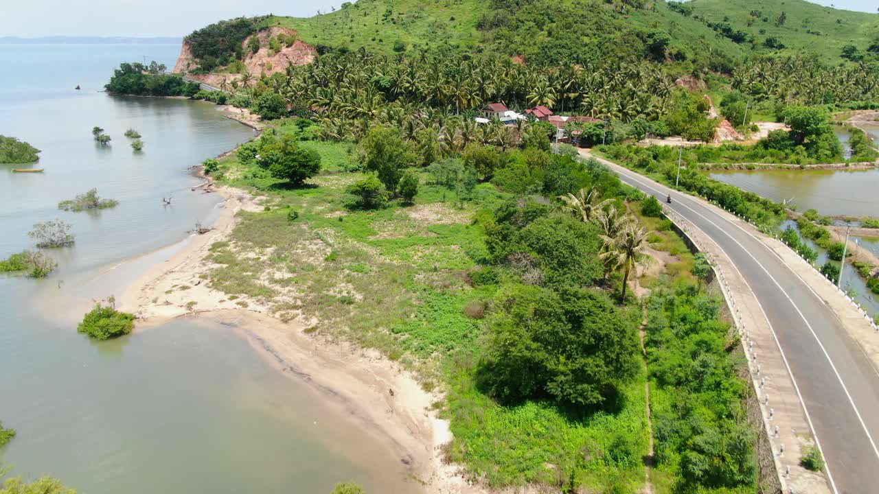 вид с воздуха, движущийся кадр, мотоцикл проезжает мимо друг друга по дороге, дома и пальмы на заднем плане