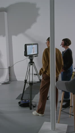 vertical video of female film director and assistant watching actors on monitor shooting movie in studio